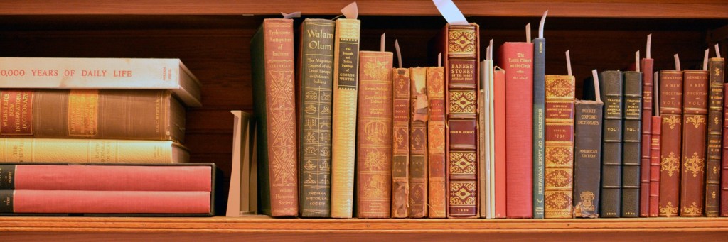 Old books on a shelf, some stacked vertically, all with paper bookmarks sticking out their tops.